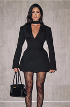 Woman wearing a black blazer dress with sheer stockings against a gray background